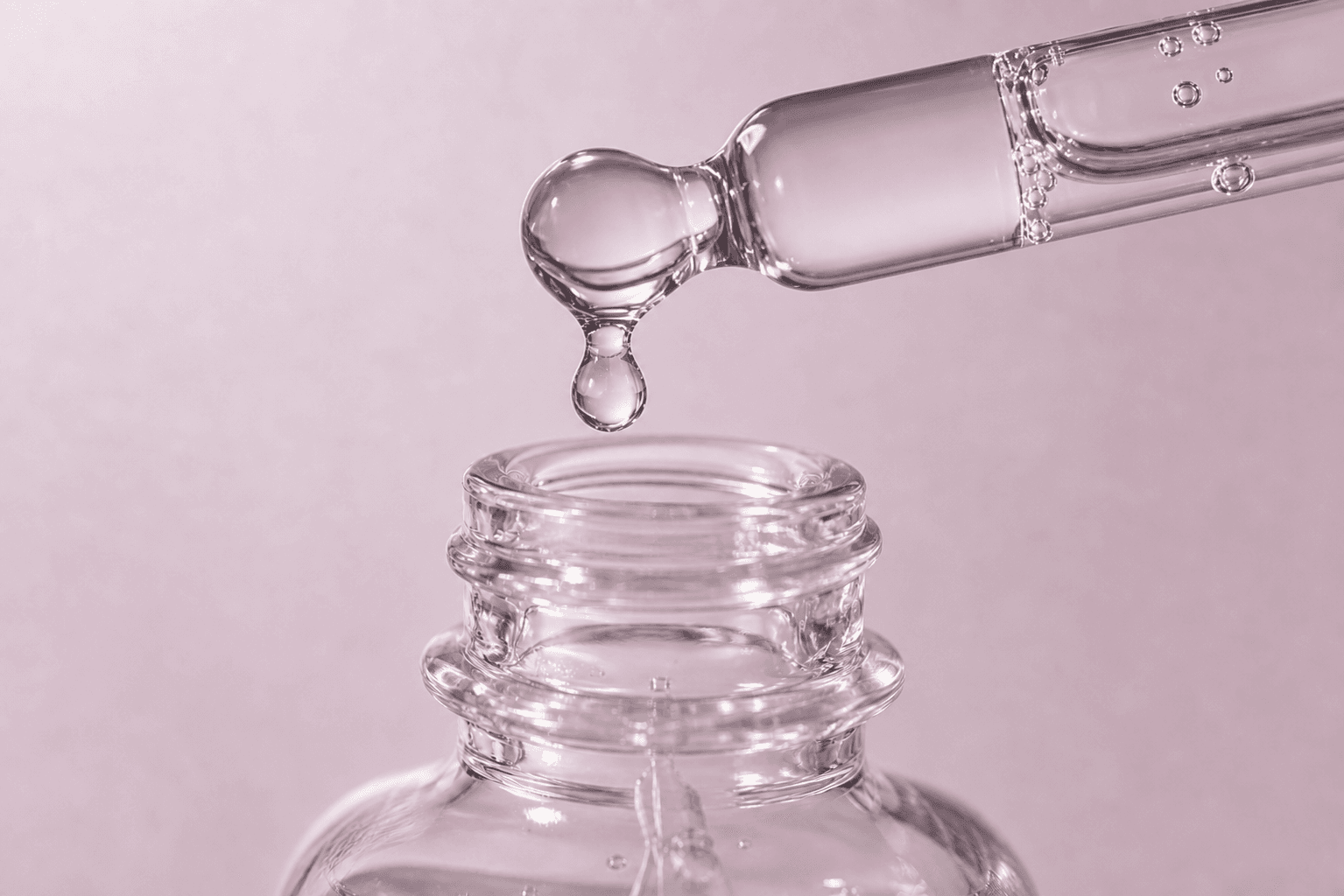 Close-up of serum dripping from a horizontal glass dropper into an open bottle